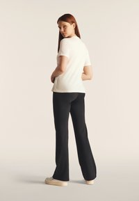 Camiseta blanca de manga corta combinada con pantalones anchos negros, vista desde atrás. Tejido suave con un diseño ajustado y proporciones simples.