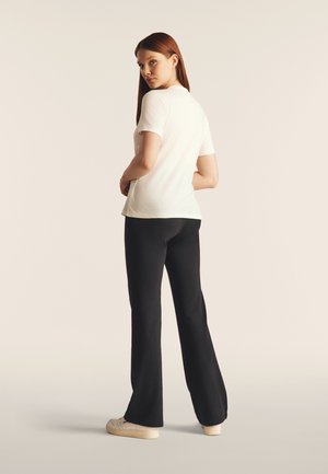 Camiseta blanca de manga corta combinada con pantalones anchos negros, vista desde atrás. Tejido suave con un diseño ajustado y proporciones simples.