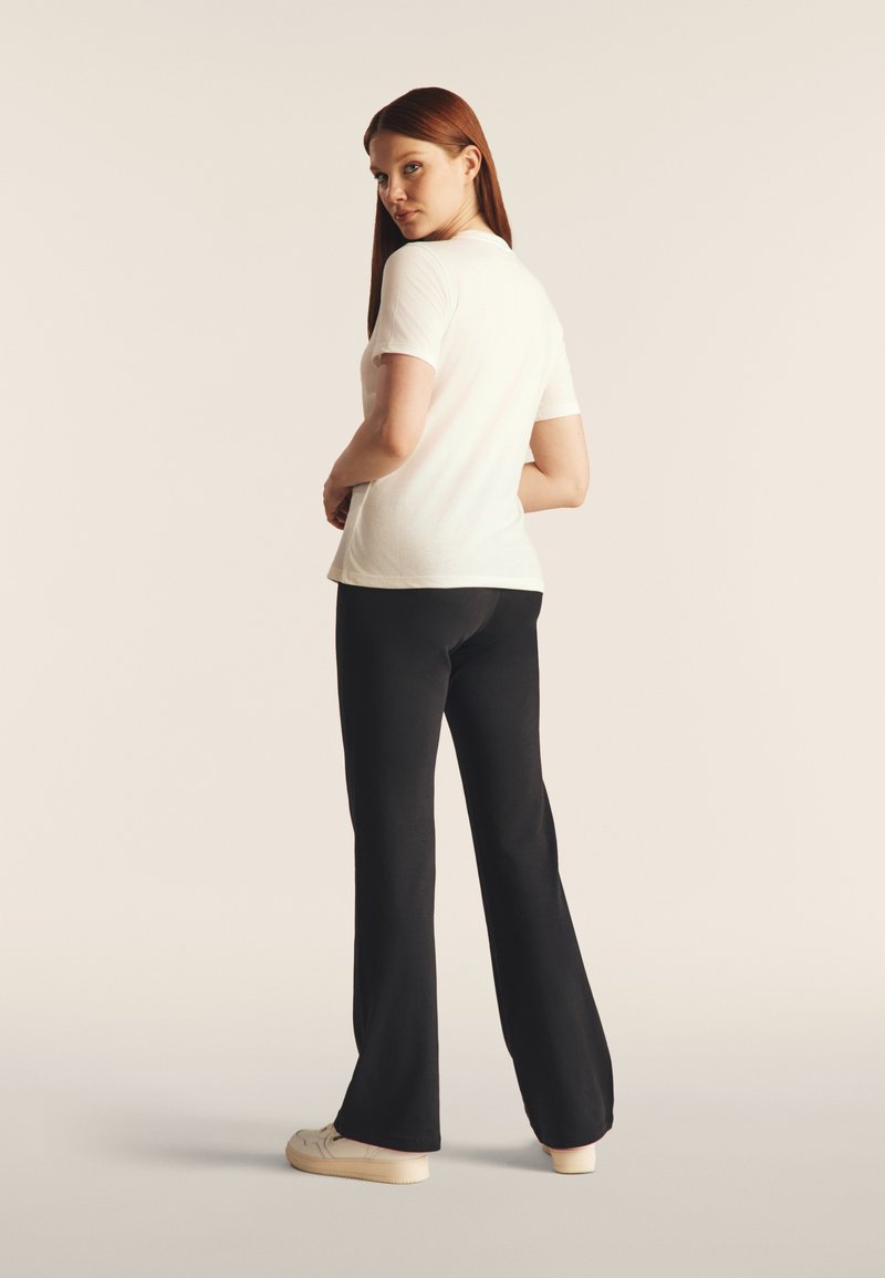 Camiseta blanca de manga corta combinada con pantalones anchos negros, vista desde atrás. Tejido suave con un diseño ajustado y proporciones simples.