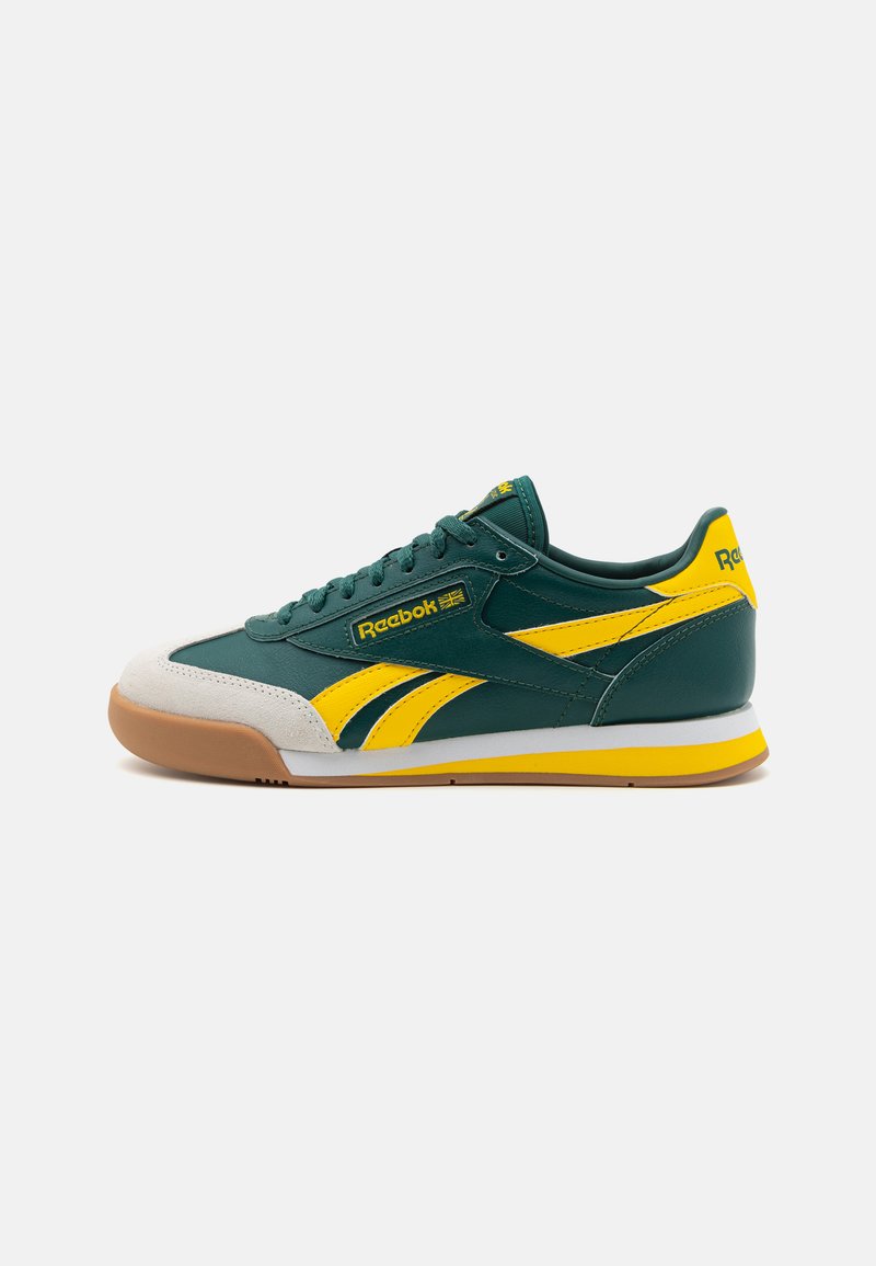 Sapatilhas verdes de couro com detalhes amarelos, bico em camurça e sola de borracha. Apresenta um design com atacadores e o logótipo da Reebok na lateral.