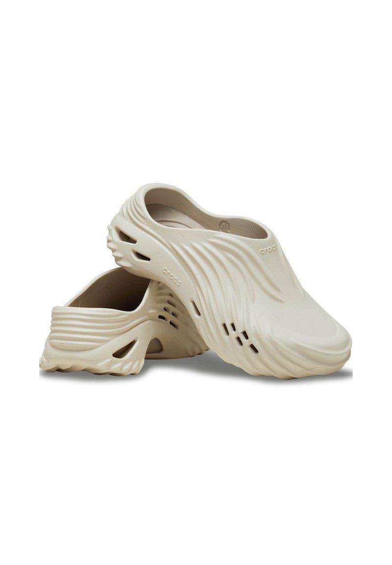 Sabots beige clair avec un design ondulé, fabriqués en matériau moulé, avec des découpes pour la ventilation et une surface texturée pour une meilleure adhérence.