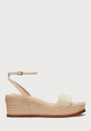 Beige Keilsandale mit Knöchelriemchen-Schnalle und gewebter Jute-Plateausohle, offenem Zehenbereich und Schlupfdesign.