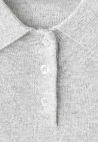 Polo shirt grigio a maglia con colletto a punta e tre bottoni bianchi. La texture è morbida e leggermente rigata.