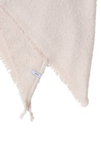 Měkká šátek světle béžové barvy s texturou ve tvaru trojúhelníku, ozdobené třásněmi na okrajích a malou bílou štítkem s nápisem "CECIL" v jednom rohu.