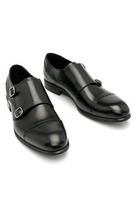 Zapatos de doble hebilla de cuero negro con dos hebillas plateadas, puntera redondeada y detalles decorativos de brogue en la puntera.
