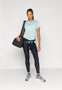 Ανοιχτό μπλε αθλητικό μπλουζάκι, μαύρα κολάν και γκρι αθλητικά παπούτσια. Μαύρη τσάντα περασμένη σε έναν ώμο, με μαύρο τοπ δεμένο γύρω από τη μέση.