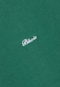 Tissu vert avec un petit logo "Blkvis" brodé en blanc en cursive, centré sur la surface.