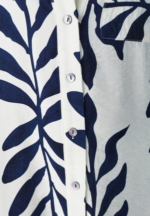 Button-up shirt featuring a white fabric with large dark blue leaf patterns. Includes a breast pocket and glossy button accents.