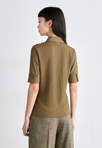 Olivenfarget stripete bluse med korte rullede ermer, kragehals og en teksturert overflate. Stylet med lysebrune bukser.