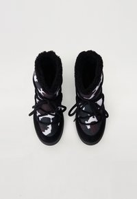 Botas de tobillo camufladas en blanco y negro con forro de felpa, cordones negros y suelas de goma, que presentan un exterior suave y texturizado.