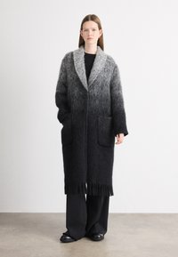 Cappotto lungo con gradiente che passa dal grigio al nero, realizzato in un materiale morbido e peloso. Presenta un colletto a scialle, due tasche e frange all'orlo.
