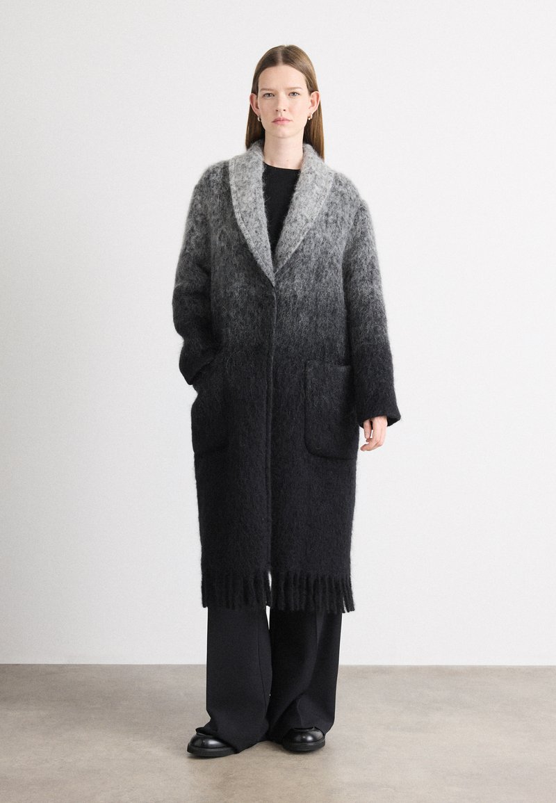 Cappotto lungo con gradiente che passa dal grigio al nero, realizzato in un materiale morbido e peloso. Presenta un colletto a scialle, due tasche e frange all'orlo.