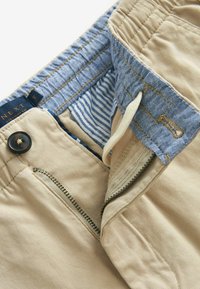 Pantaloni beige a taglio dritto con una cintura in denim blu, caratterizzati da una fodera a righe, zip in metallo e chiusura con bottone nero.
