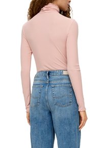 Lange mouw, roze coltrui met een ruche rond de hals, gecombineerd met hoog-gesneden blauwe jeans met twee achterzakken en stikdetails.