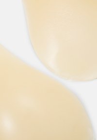 Semelles en silicone beige avec une surface lisse et légèrement brillante, présentant une forme contourée et un texturage subtil pour le confort.