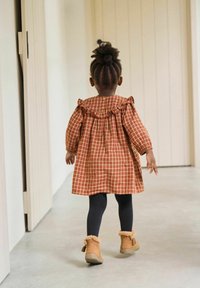 Rot-beige karierter Kleid mit rüschigem Ausschnitt, langen Ärmeln, getragen mit schwarzen Leggings und beigen Stiefeln, von hinten betrachtet.