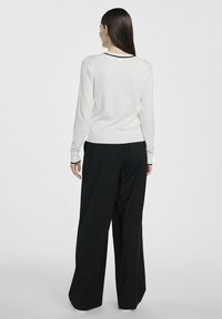 Biała dzianinowa bluzka z długim rękawem z czarnym wykończeniem przy dekolcie, w połączeniu z luźnymi czarnymi spodniami. Posiada subtelny akcent na plecach w okolicy dekoltu.