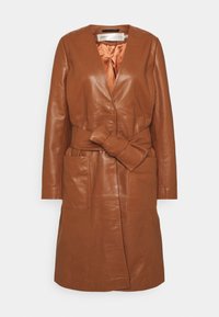 Brun läderjacka med djup V-hals, långa ärmar, en knuten rosett i midjan och stora framfickor. Fodrad med orange satin.