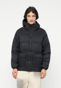 Μαύρο μπουφάν τύπου puffer με εφαρμοστό καπέλο, φερμουάρ και δύο μπροστινές τσέπες τύπου patch. Διαθέτει σχέδιο με πλέγμα και ελαστικά μανίκια.
