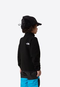 Jachetă fleece neagră cu guler înalt, cu logo-ul The North Face. Asortată cu pantaloni negri și albaștri, căciulă caldă cu urechi și căptușeală din blană.