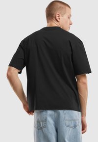 Černé oversized tričko z bavlny, s krátkými rukávy a kulatým výstřihem. Zadní pohled ukazuje hladkou texturu a uvolněný střih.
