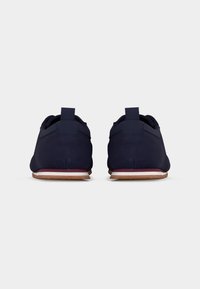 Paire de baskets décontractées bleu foncé vues de dos avec semelles en caoutchouc marron et accents blancs et rouges sur la semelle intermédiaire sur fond blanc.