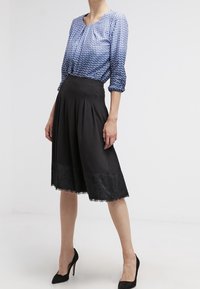 Blusa de estampado azul claro con mangas tres cuartos, combinada con una falda negra a la altura de la rodilla con un borde de encaje en el dobladillo. Tacones altos negros.