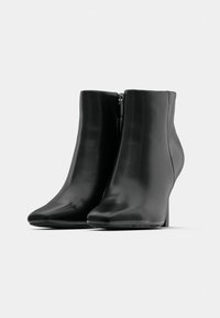 Botas de tornozelo pretas com um material elegante e brilhante, bico fino e um fecho lateral discreto. O salto tem uma altura moderada e é texturizado.
