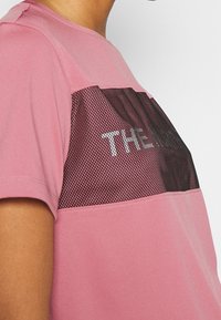 Camiseta atlética rosa con un panel de malla negro con "THE" impreso en blanco, de manga corta y textura suave.