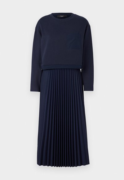 Marineblaues Kleid mit einem taillierten Langarm-Top und einer aufgesetzten Tasche über einem plissierten Rock. Glatte Stoffoberfläche, einfaches Design.