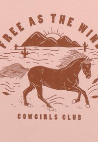 Rosa T-Shirt mit einer braunen grafischen Illustration eines rennenden Pferdes, Bergen und Kakteen, sowie dem Text "FREI WIE DER WIND" und "COWGIRLS CLUB."