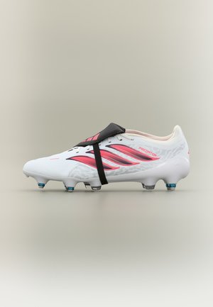 Białe i różowe korki piłkarskie Adidas Predator z czarnym paskiem nad sznurowadłami i niebieskimi ćwiekami na neutralnym tle.