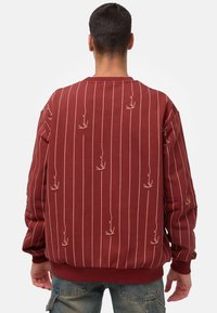 Sudadera roja con rayas verticales y un sutil diseño bordado. Incluye puños y dobladillo acanalados, y un corte relajado.