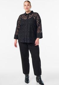 Čierna čipkovaná polokošeľa s golierom a trojštvrťovými rukávmi. Spárovaná s čiernymi nohavicami a členkovými topánkami na vysokom podpätku s cvočkovými akcentmi.