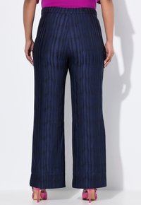 Široké kalhoty v námořnické modři s vertikální texturou pruhů, s elastickým pasem a hladkým materiálem. Doplněné růžovými vysokými podpatky.