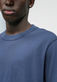 Μπλε φούτερ από βαμβάκι με στρογγυλή λαιμόκοψη, εμφανή ραφές και λεία υφή; χωρίς γραφικά σχέδια. Λήψη κοντινής θέας.