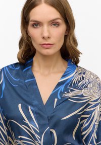 Robe di seta di un blu intenso con motivi floreali bianchi e azzurri. Presenta un colletto a scialle e una texture liscia, coprendo le spalle.