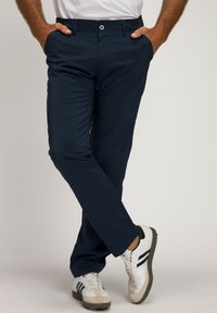 Pantaloni blu navy con una texture liscia, taglio slim, tasche laterali, vita elasticizzata e chiusura con bottone argentato, abbinati a scarpe sportive bianche.