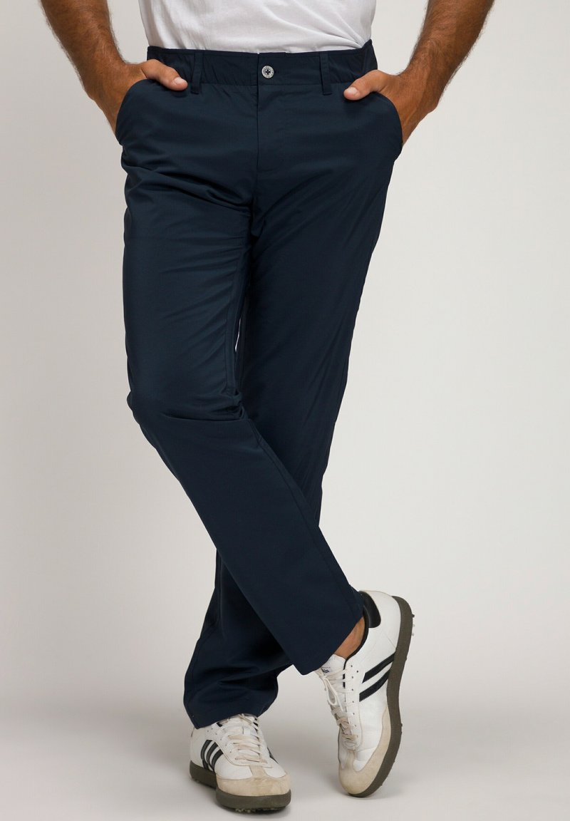 Pantaloni blu navy con una texture liscia, taglio slim, tasche laterali, vita elasticizzata e chiusura con bottone argentato, abbinati a scarpe sportive bianche.