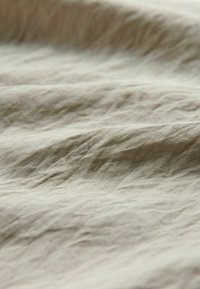 Jasnobeżowa teksturowana tkanina o pomarszczonym wyglądzie, charakteryzująca się miękkim, cienkim splotem i subtelnymi nieregularnymi wzorami.