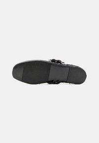 Svart sandal med en texturerad gummisula, med justerbara remmar och dekorativa detaljer. Designen fokuserar på komfort och stabilitet.