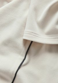 Bela športna majica iz gladkega blaga z teksturirano površino, s črnim šivom ob strani za dodaten dizajn.