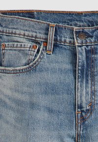 Jeans din denim albastru deschis cu talie înaltă, prezentând nituri din cupru, cusături în contrast și o mică buzunar frontal.