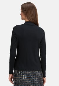 Schwarzes Langarmoberteil mit gerippter Textur und gewelltem Saum, kombiniert mit einem gemusterten Tweedrock. Von hinten betrachtet, zeigt es ein glattes, eng anliegendes Design.
