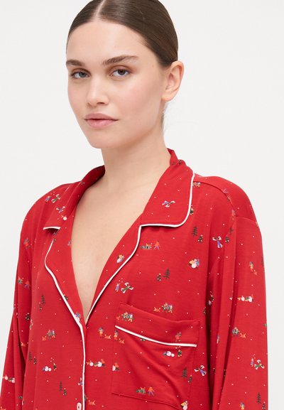 Camisola de pijama vermelha feita de um tecido suave, com um bolso e bainha branca. O padrão apresenta ilustrações coloridas com tema de inverno.