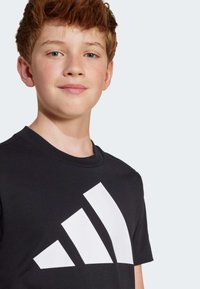 T-shirt en coton noir avec un grand logo blanc à trois bandes sur le devant. Encolure ronde simple et manches courtes.