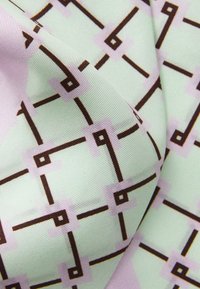 Tkanina so vzorom, na ktorej je svetlo mäta zelené pozadie s geometrickým dizajnom hnedých línií a fialových štvorcov. Hladký povrch.