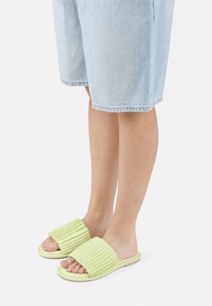 Grønne gummiklippesandaler med et ribbet overdesign. Synlig flat såle og åpen tå. Brukt med lyse denimshorts.