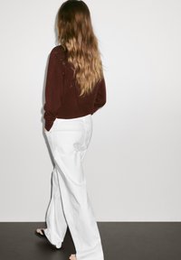 Burgundský svetr spárovaný s bílými širokými kalhotami, které mají uvolněný střih a měkkou texturu, s hladkým povrchem a minimálními detaily.