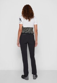 Black outdoor pants are paired with a white and olive green shirt featuring a geometric pattern. The pants have a fitted design and a practical waist.
